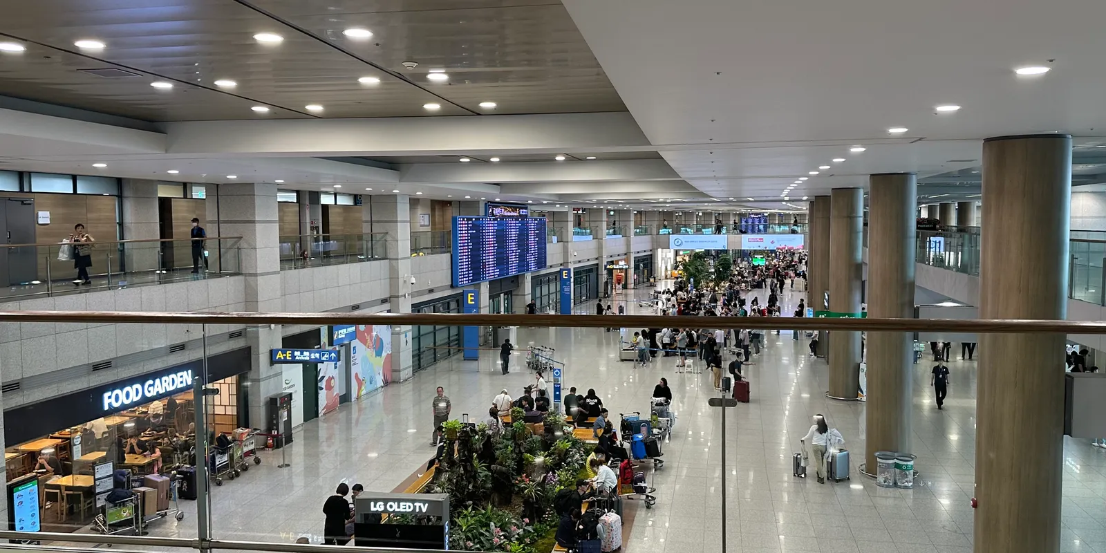 The first-floor arrivals hall of Incheon International Airport Terminal 1 seen from the railing above, with the A–E arrivals sign and the Food Garden