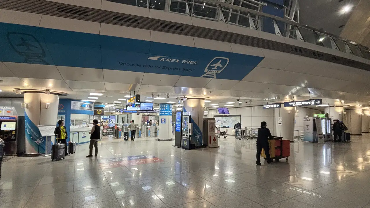 The AREX all-stop train concourse at Incheon Airport Terminal 1 station, with ticket machines and fare gates and travelers passing with suitcases