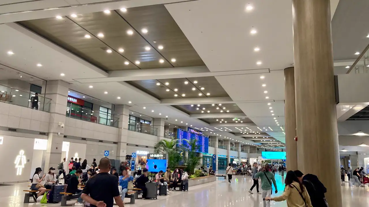 Arrivals lobby of Incheon International Airport Terminal 1, with travellers resting on benches and an arrivals board in the distance
