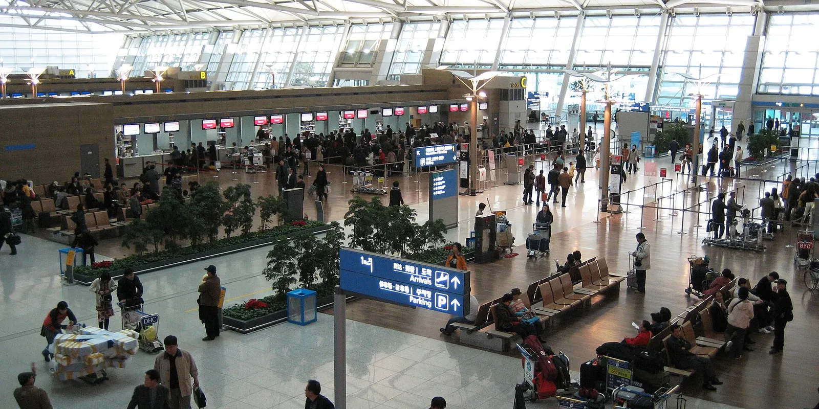 上の階から見下ろした仁川国際空港の出発ロビー。チェックインカウンターに並ぶ旅行者と、荷物カートの横のベンチに座る人たち