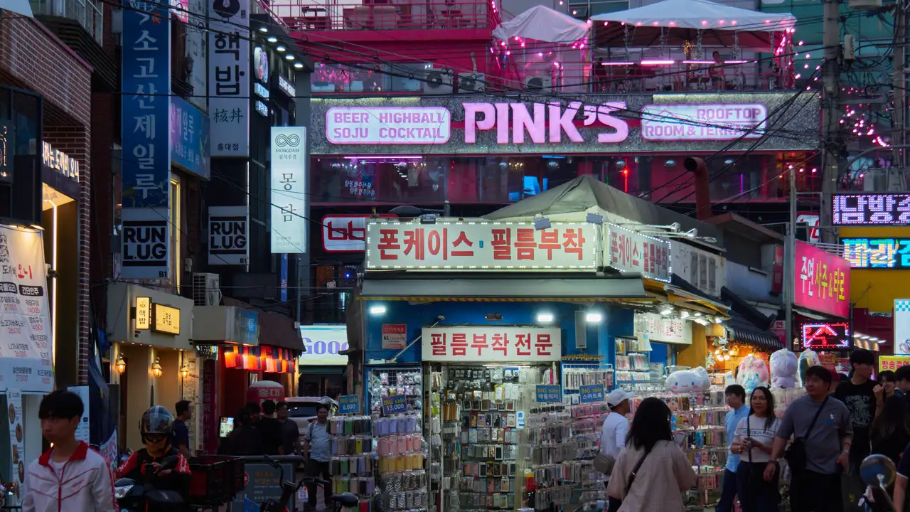 A Hongdae street in Seoul at night, with a phone case and screen protector stall under neon signs