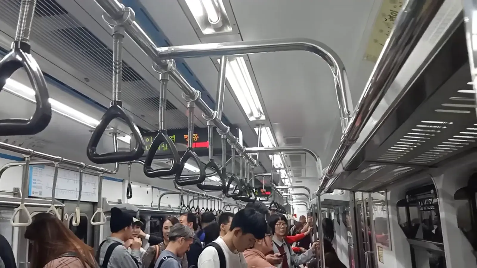 Inside a Seoul Metro Line 4 car, passengers standing under a row of hand straps
