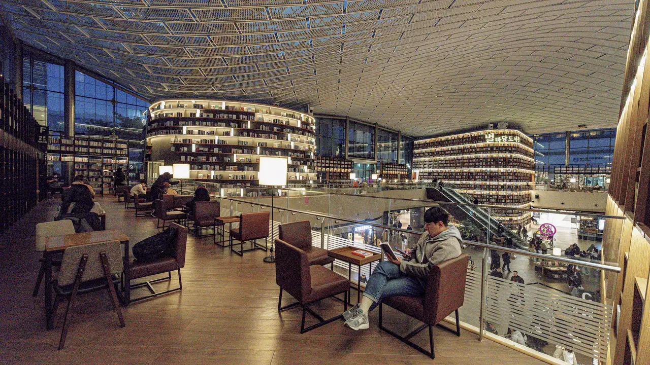 Second-floor lounge of Starfield Library at COEX in Seoul, a person reading in a leather armchair with curved bookshelves behind